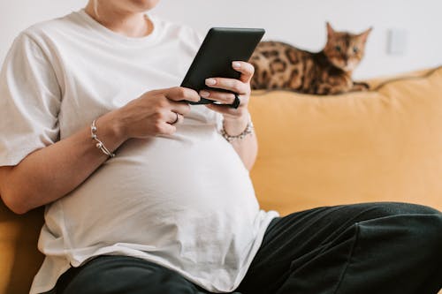 Free Pregnant Woman in White Shirt Holding a Tablet Stock Photo