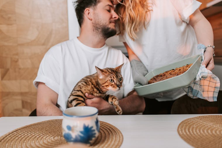 A couple enjoys a cozy moment indoors with their Bengal cat and a freshly baked pie.