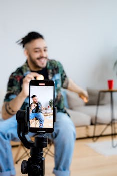 A young man vlogs indoors with a smartphone on a tripod, capturing engaging content.