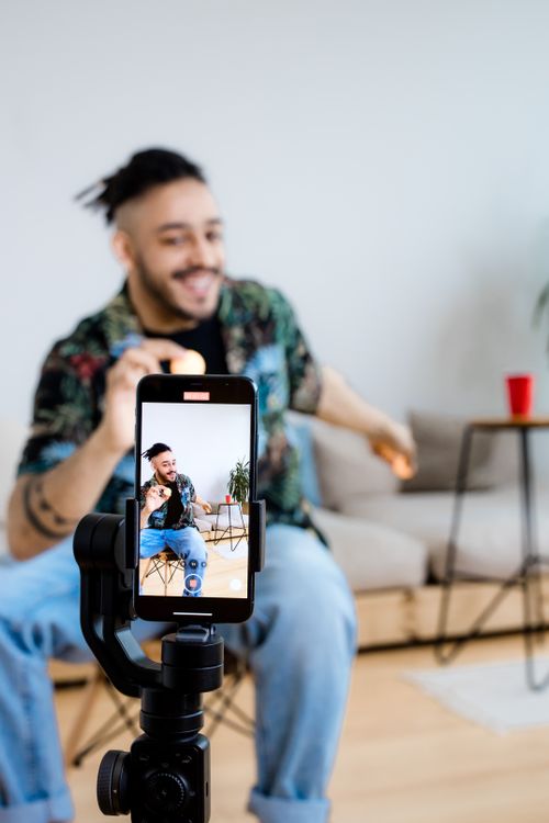 Free A young man vlogs indoors with a smartphone on a tripod, capturing engaging content. Stock Photo