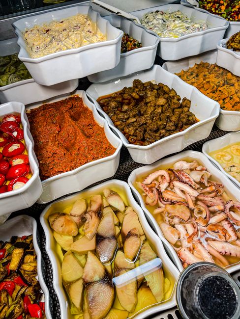 A variety of marinated and prepared foods displayed in white trays at a deli counter.
