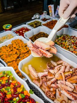 Close-up of a serving spoon with fresh octopus at a colorful buffet.
