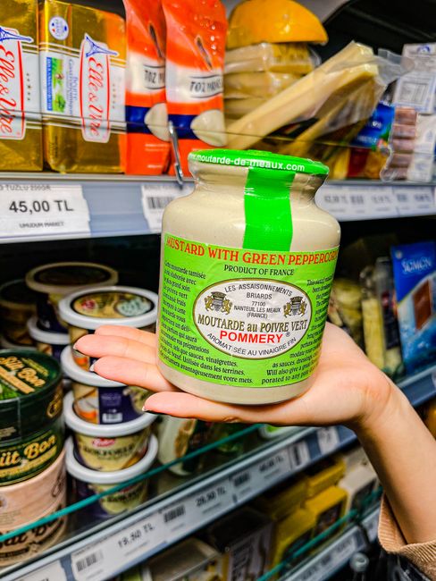 A person holding Pommery mustard jar in a grocery aisle shelf. Perfect for food and retail themes.