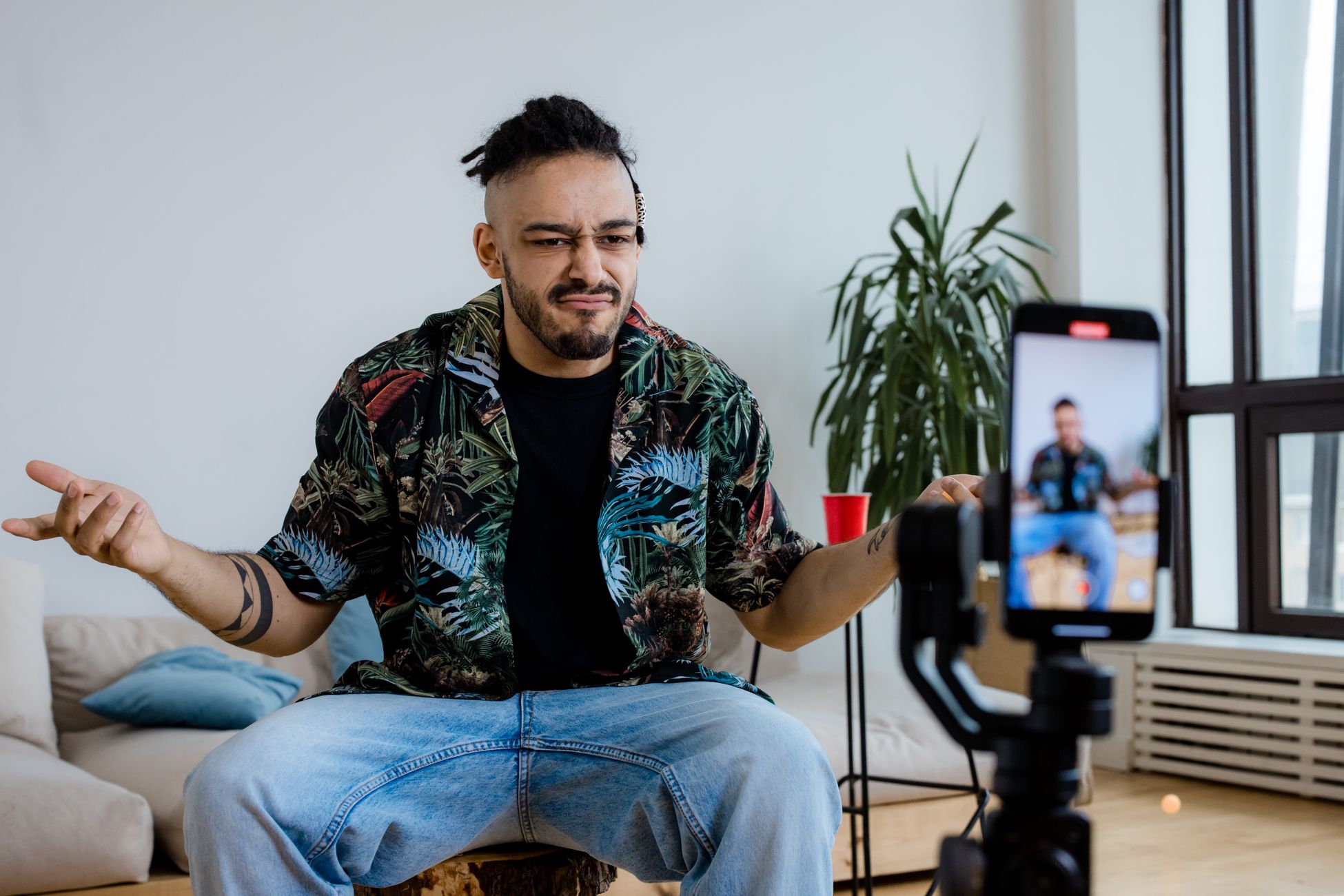 Casual man vlogging in a modern living room using smartphone on tripod, expressing thoughts.