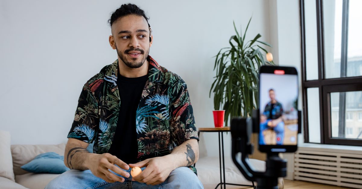 A young man recording video content indoors with a smartphone and tripod.