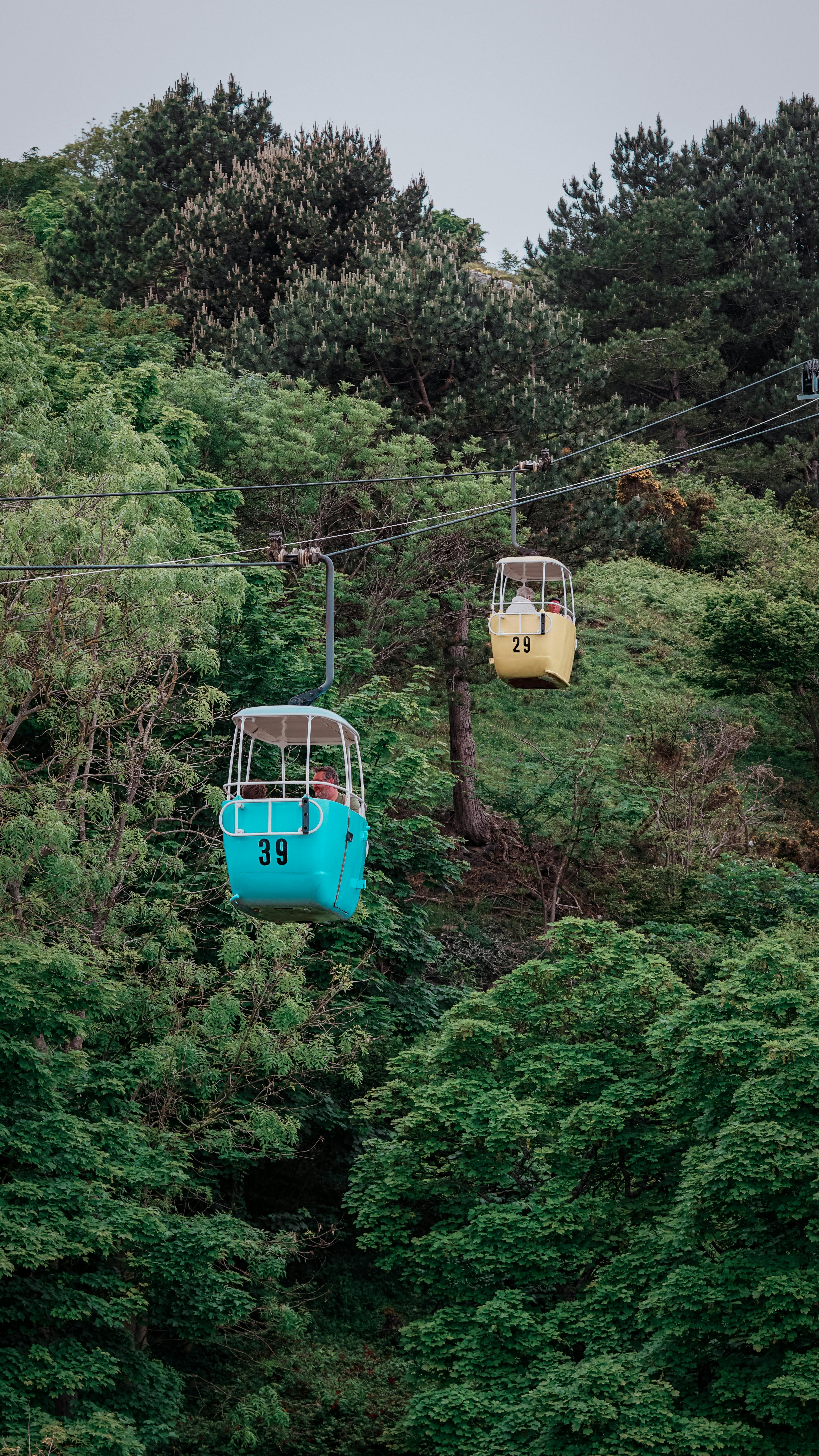 Two vibrant cable cars glide over Llandudno's verdant hills, showcasing nature and adventure.
