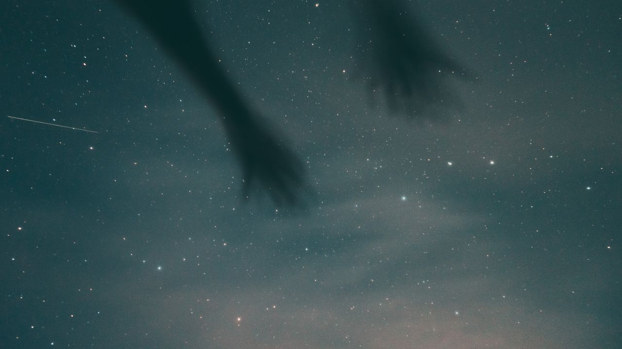 a mysterious night sky with shadowy hands and stars creates a surreal