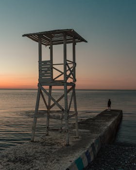 A serene sunrise at a lifeguard tower in Sochi with a lone person on a breakwater.
