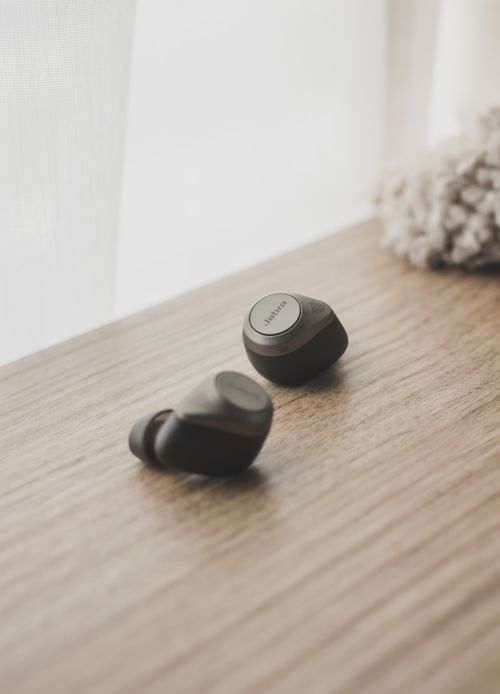 Free Close-up of sleek wireless earbuds resting on a stylish wooden surface by a window. Stock Photo