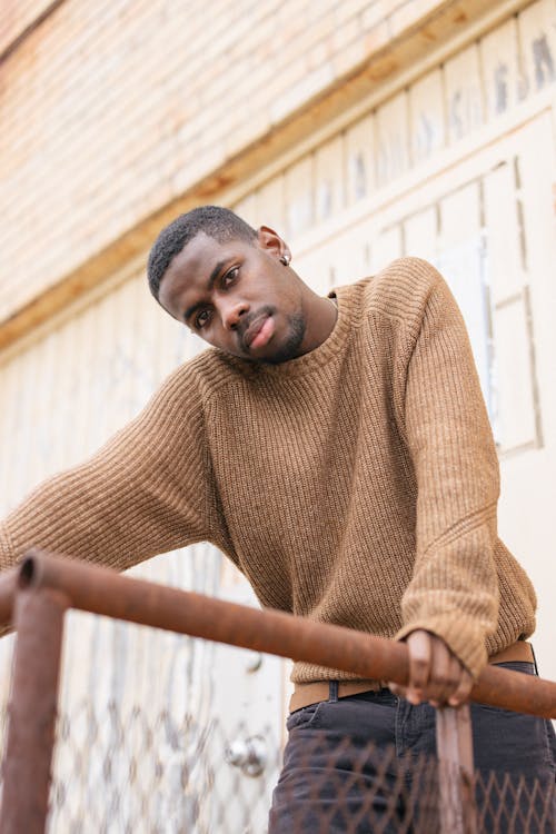 Man in Brown Sweater Standing and Leaning on Brown Wooden Railings