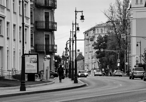Free A black and white street scene featuring historic architecture, street lights, and pedestrians. Stock Photo