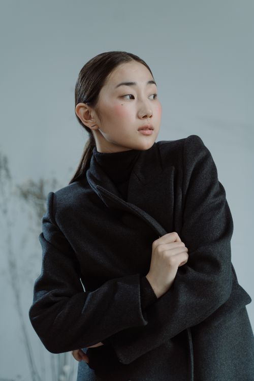 Free Portrait of an Asian woman wearing a dark coat, looking away in a modern fashion pose. Stock Photo
