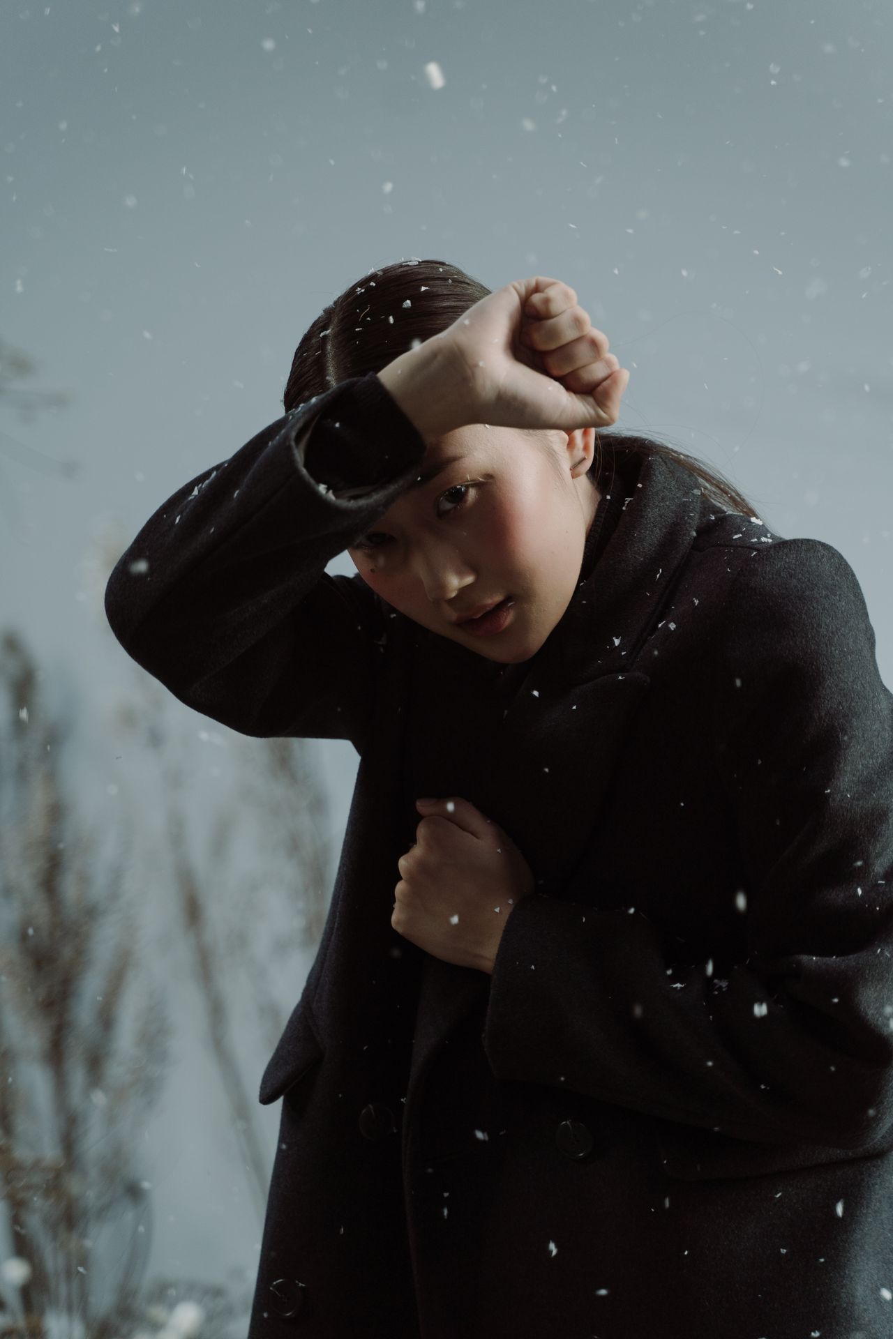 Woman in a black coat bracing against falling snow