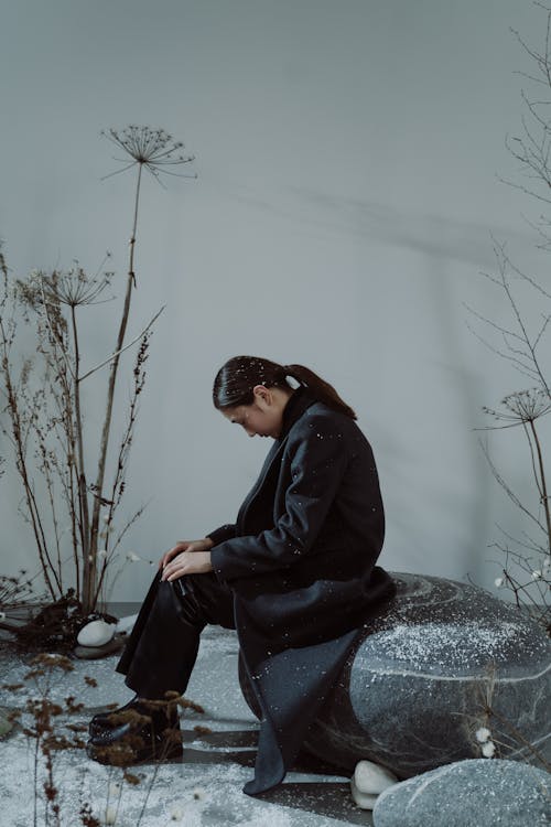 A Woman Wearing a Black Coat and Sitting on a Rock