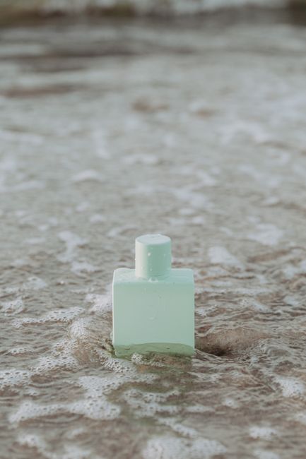Minimalist perfume bottle resting on the sandy beach surrounded by ocean waves.