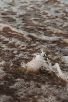 A serum bottle surrounded by small ocean waves and foam.