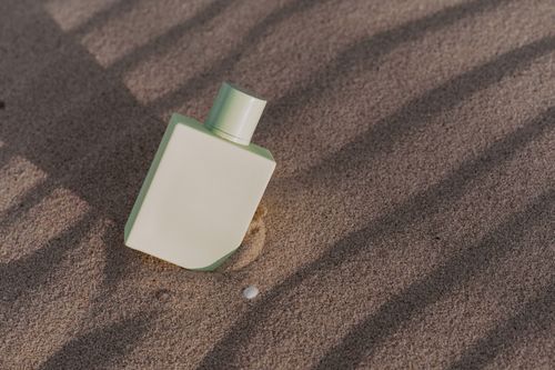 Free A minimalist perfume bottle partially buried in summer beach sand, casting artistic shadows. Stock Photo