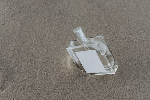 Free Minimalist perfume bottle resting on textured sand, capturing elegance and simplicity. Stock Photo