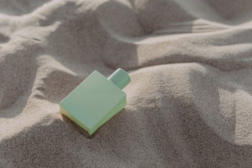 Close-Up Shot of a Green Perfume Bottle on the Sand