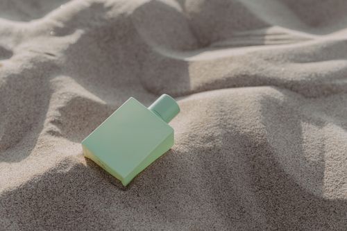 Free A sleek green perfume bottle rests on sand, showcasing elegance and simplicity. Stock Photo