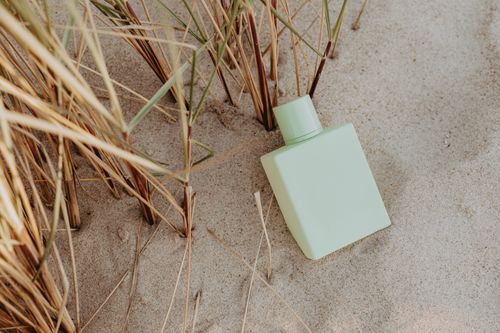 Free A minimalist perfume bottle placed on sandy beach surrounded by dry grass. Stock Photo