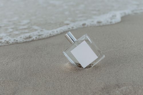 Free A stylish perfume bottle resting on sandy beach near the shoreline, evoking a sense of luxury and tranquility. Stock Photo