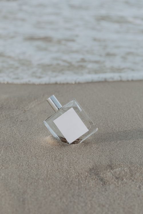 Free Close-up of a perfume bottle on the seashore with waves in the background, perfect for product promotions. Stock Photo