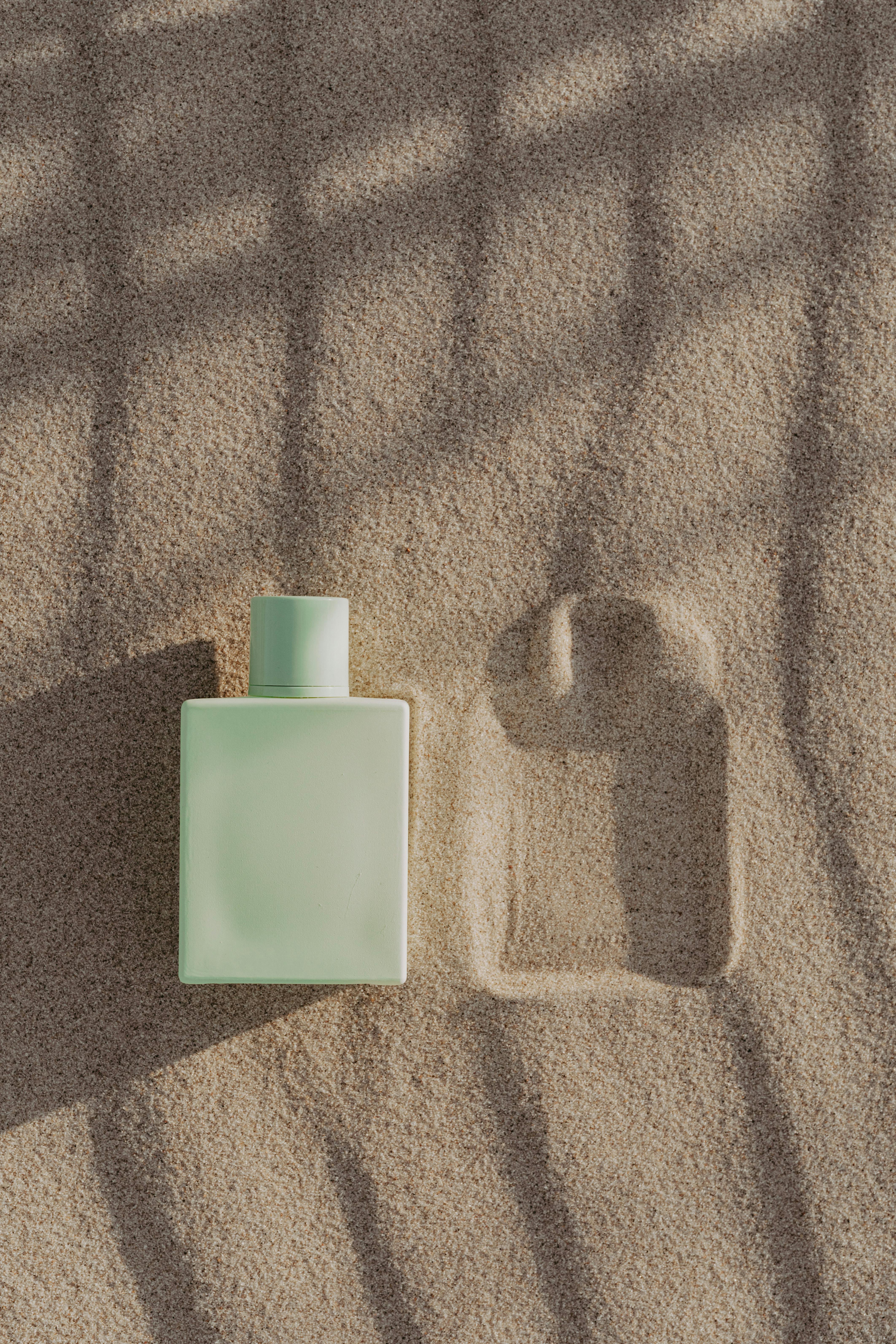 close up shot of a green perfume bottle on the sand