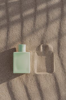 A minimalist perfume bottle captured in warm sand with shadows, creating an artistic product photo.