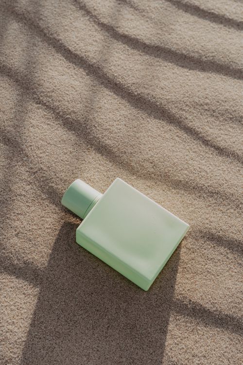 Free Elegant green perfume bottle resting on textured sand, evoking a serene and natural aesthetic. Stock Photo
