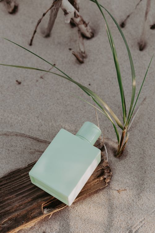 Free A close-up of a minimalist perfume bottle displayed on a sandy beach with greenery. Stock Photo