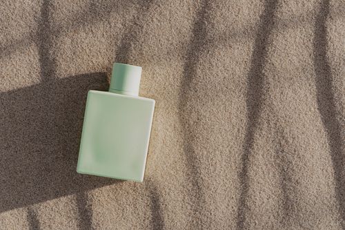 Free Flat lay of a minimalist green perfume bottle on textured sandy surface. Stock Photo
