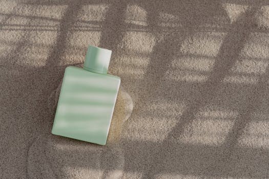 A sleek perfume bottle placed on sand with dramatic sunlight and shadow patterns, perfect for stylish product presentations.