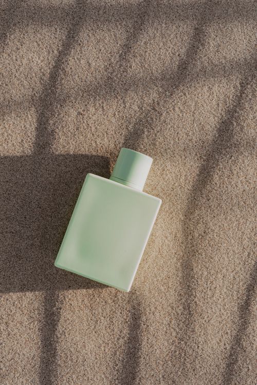 Free A minimalist green perfume bottle elegantly positioned on textured sand for a chic, natural feel. Stock Photo