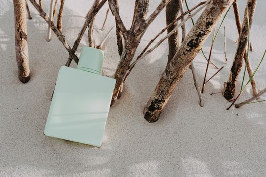 A green perfume bottle artistically placed on sand amidst dry branches, creating a minimalist style.
