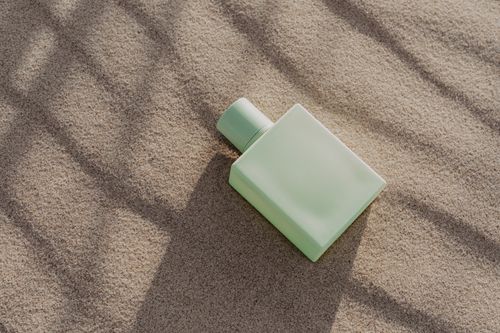 Free A minimalist perfume bottle lies elegantly on sand, casting soft shadows in natural light. Stock Photo