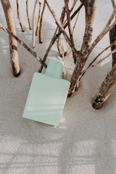 A sleek perfume bottle nestled among branches on a sandy beach, creating a unique natural display.