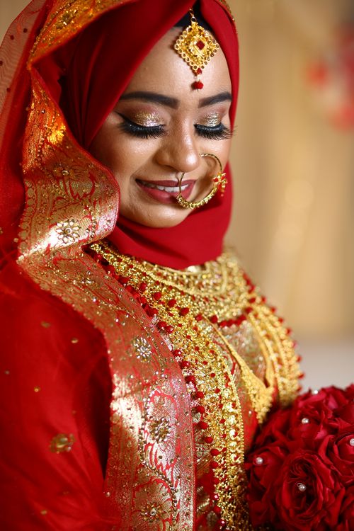 Free Stunning portrait of a bride in intricate red and gold traditional clothing with a bouquet. Stock Photo