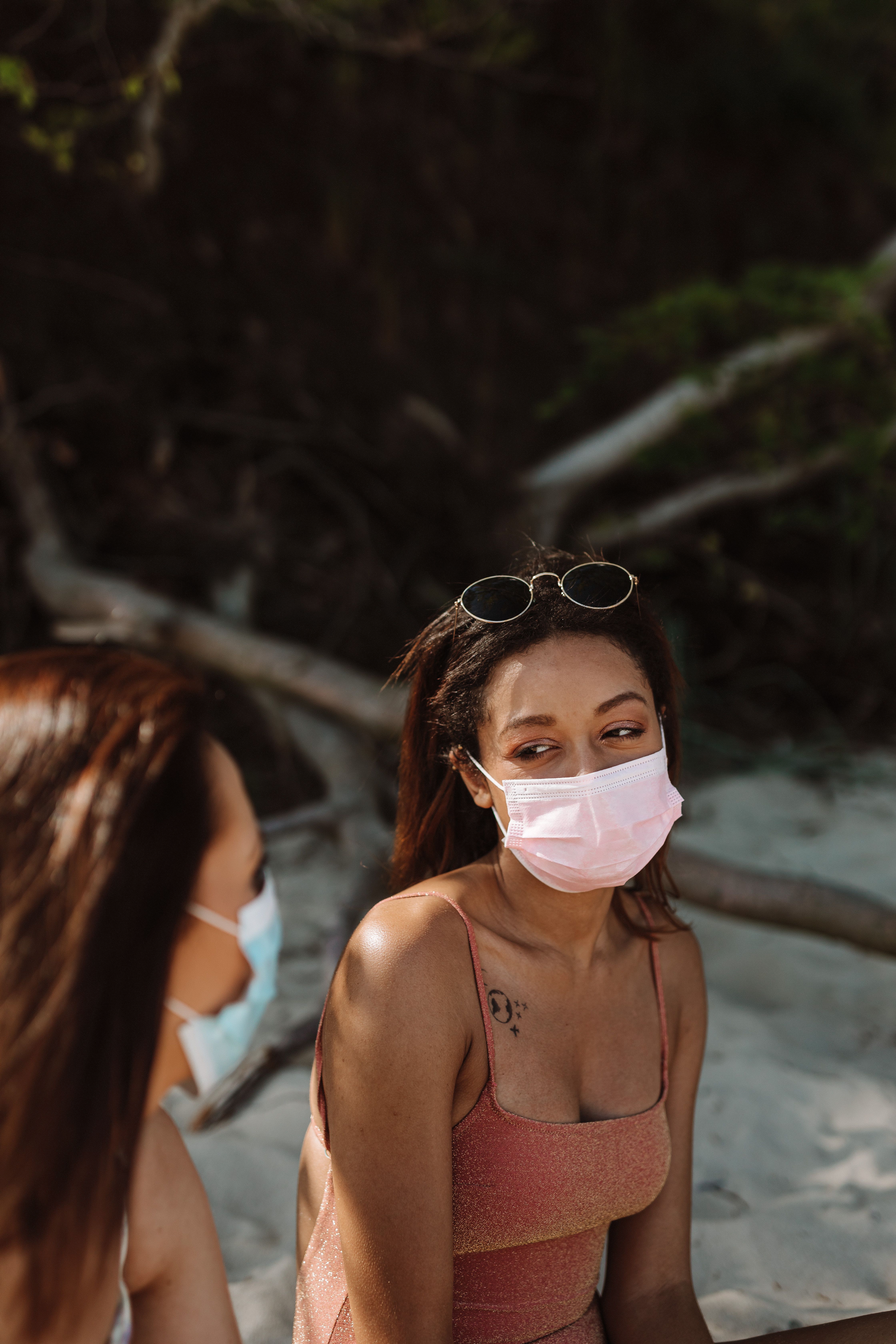 Two women wearing face masks, enjoying a sunny day at the beach while practicing safety measures.