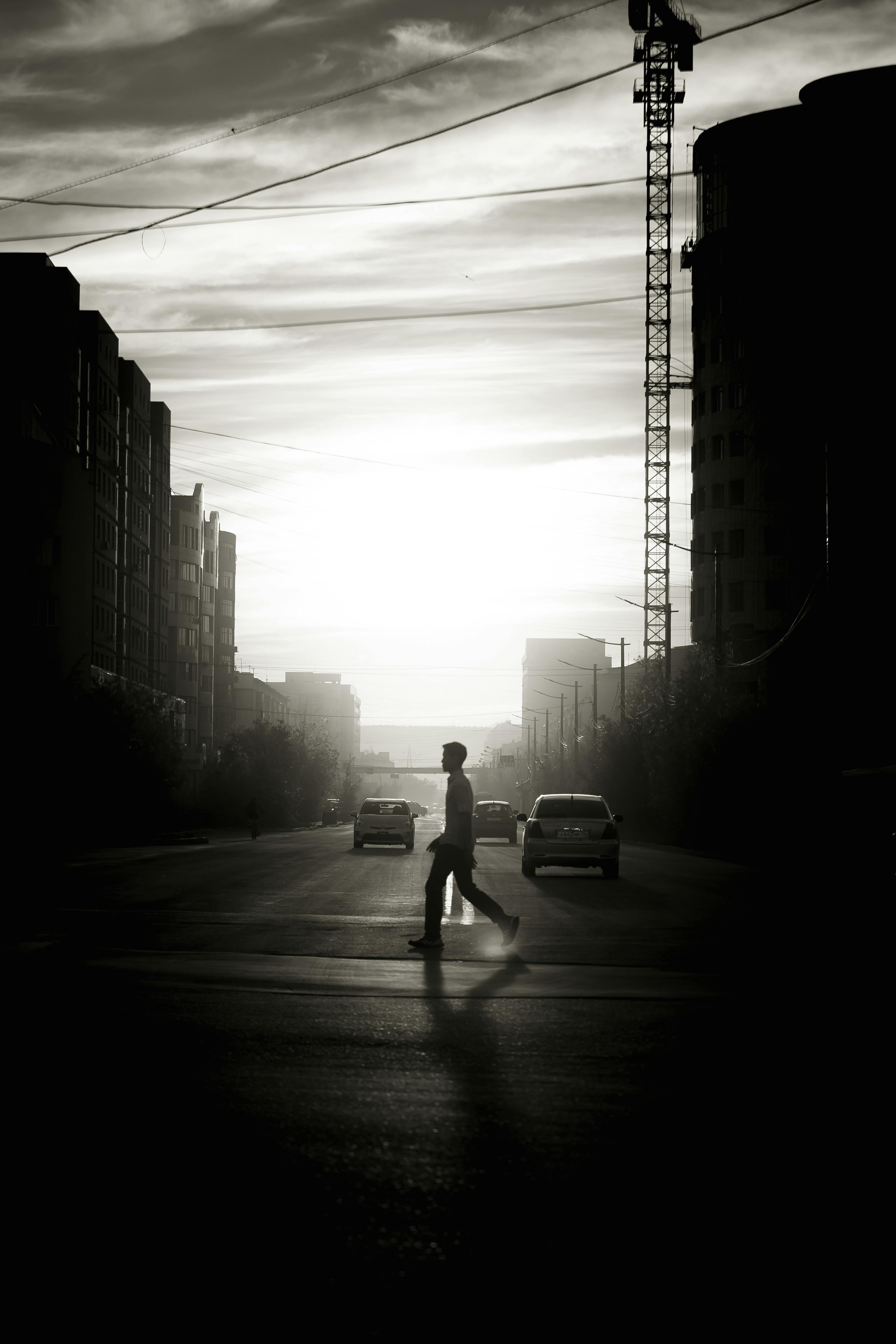 A man walks across the road in a city during sunset, casting a prominent shadow.
