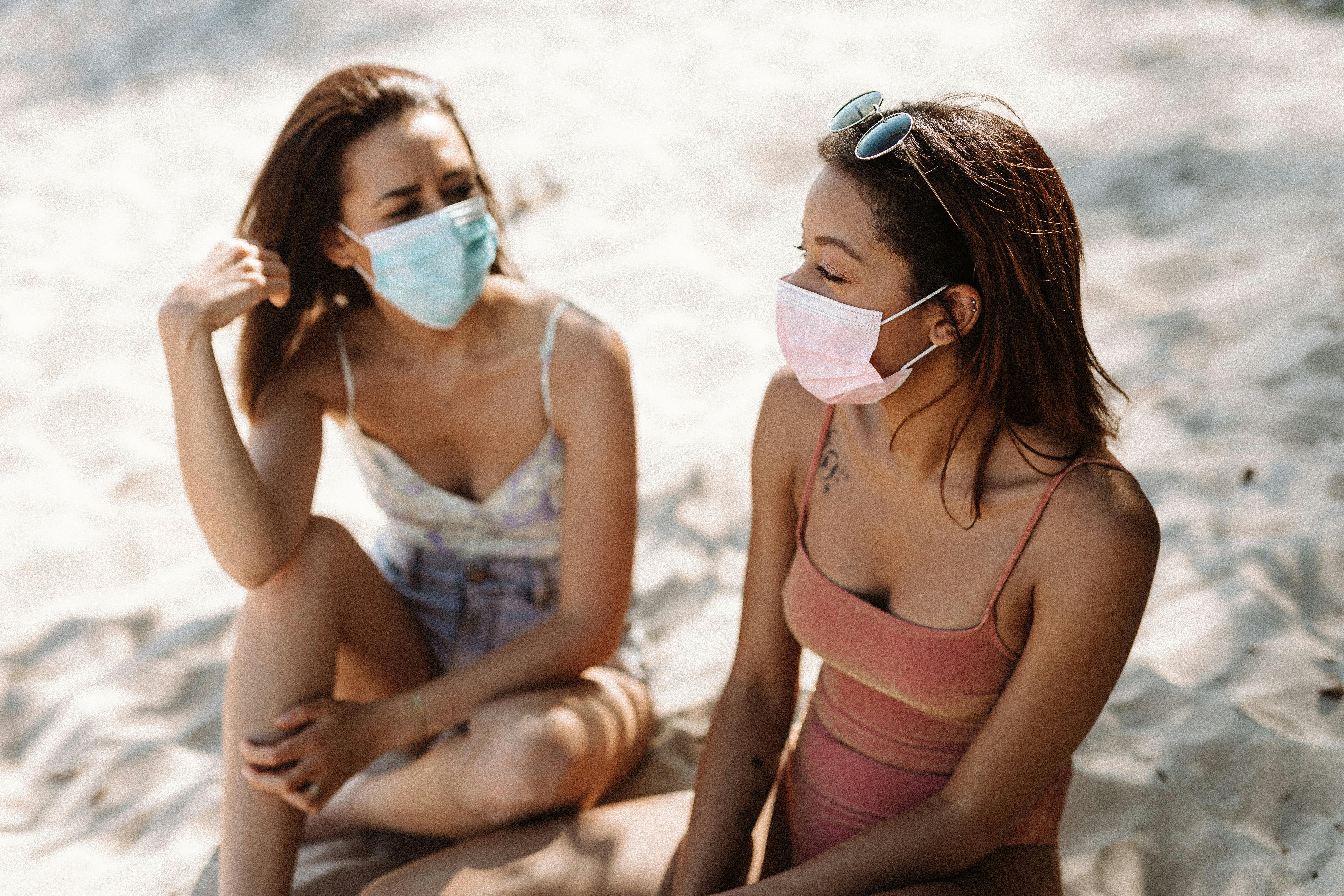 Two women wearing face masks enjoying a sunny beach day.
