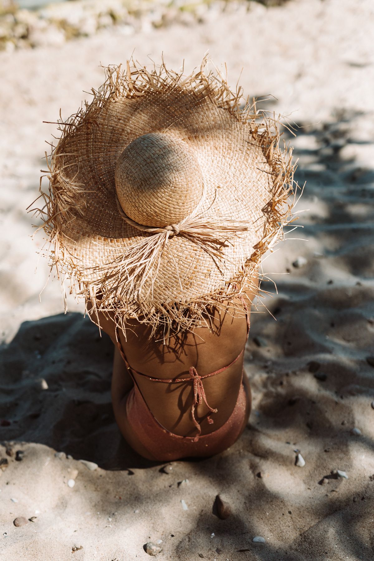 A woman in a sunhat sitting on the sand — the unhurried ease of summer