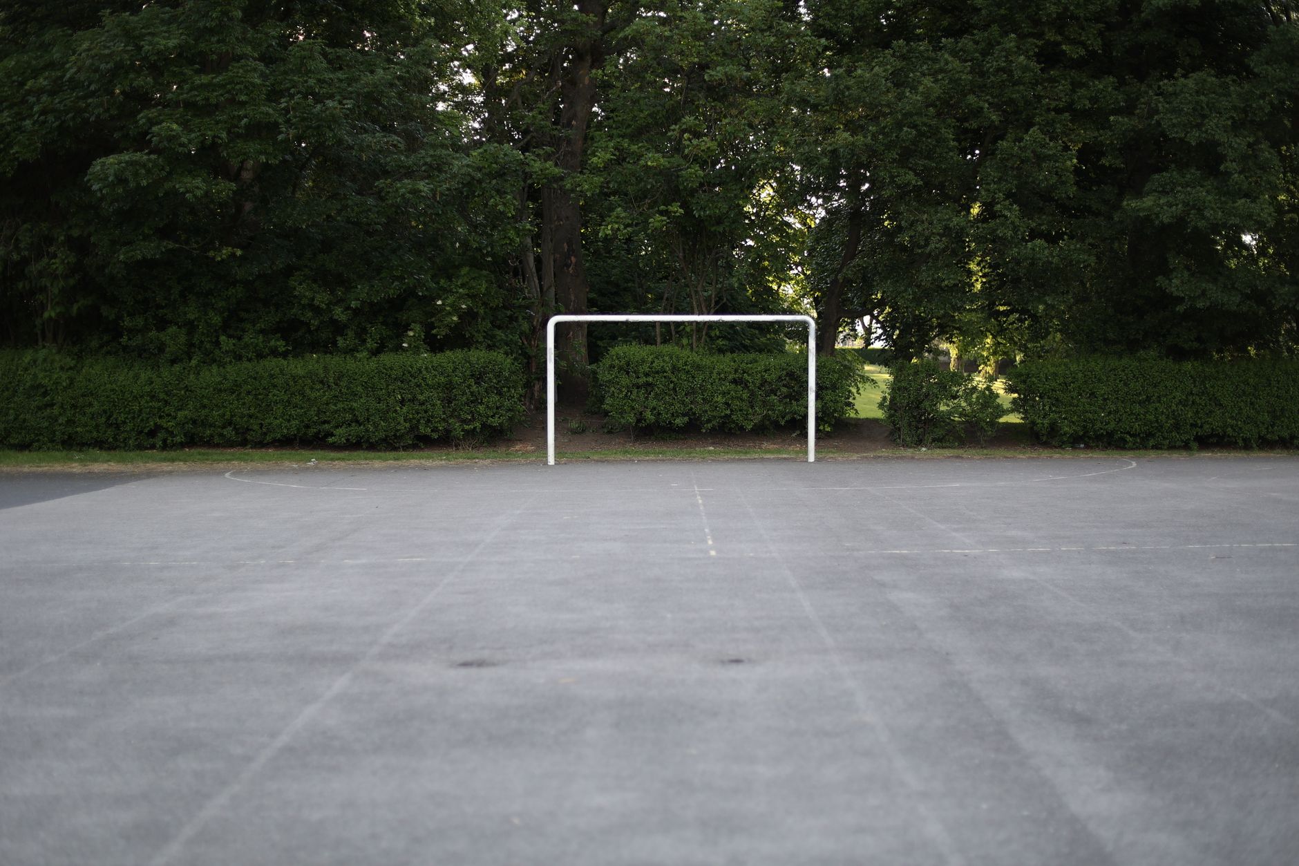 Empty concrete soccer field with a goal surrounded by lush trees in Bradford, England.