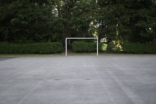 Empty concrete soccer field with a goal surrounded by lush trees in Bradford, England.