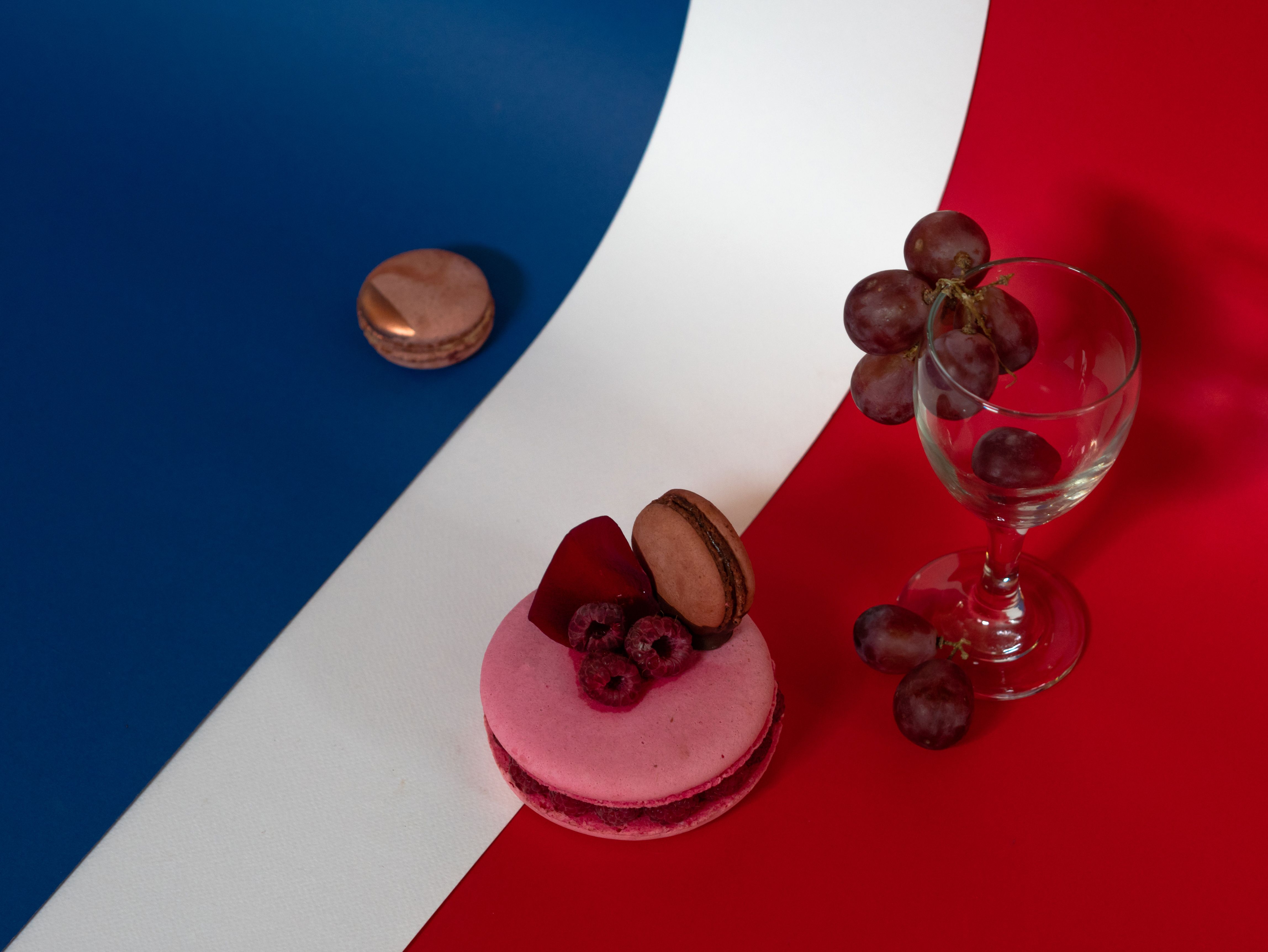 A colorful arrangement of macarons, grapes, and a wine glass on a French flag background.