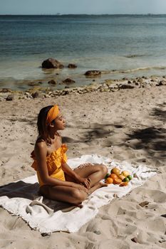 Serene moment of a woman in an orange swimsuit sitting on a beach alongside tropical fruits.