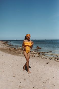 Woman in yellow swimsuit walking along a serene beach on a sunny day, enjoying the ocean view.