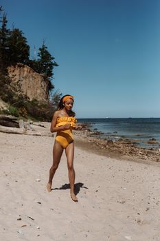 A woman in a yellow swimsuit strolls leisurely on a sunlit beach, surrounded by clear blue skies and calm seas.