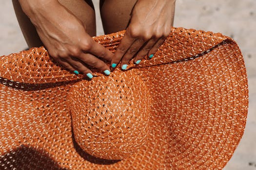 Detailed shot of hands with blue nails holding a woven sun hat outdoors.