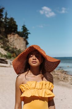 Woman in a wide-brimmed hat enjoying a sunny day at the beach with a bright blue sky.